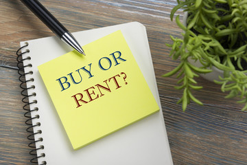 Real estate concept. Notepad with buy or rent message, pen and flower. Office supplies on desk table top view