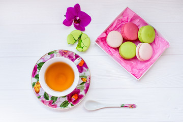 Color macaron and cup of tea on a white wooden background. Flat lay