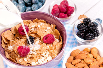 healthy breakfast with cornflakes berries, milk and almond nuts on wooden table