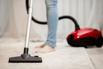 Woman doing house cleaning, vacuuming carpet with thick pile