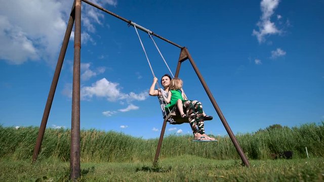Adorable little girl with her beautiful mother having fun on a swing outdoor
