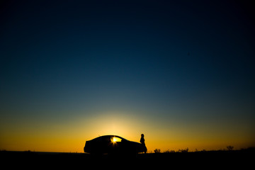 Fototapeta na wymiar Silhouette of sedan car with girl on the background of beautiful sunset
