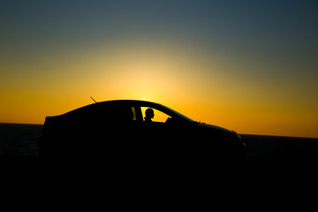 Naklejka na ściany i meble Silhouette of sedan car with girl on the background of beautiful sunset