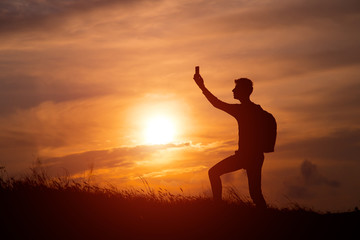 Fototapeta premium Silhouette of tourist man spread hand on top of a mountain enjoying sunset