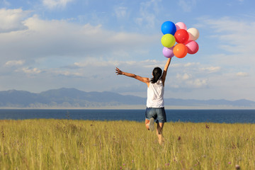 cheering young asian woman on grassland with colored balloons