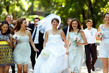 Smiling bride walks in happy crowd of friends in the park