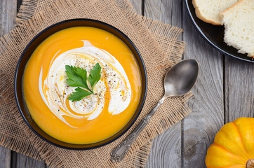 Pumpkin soup with cream and parsley on wooden background, top view