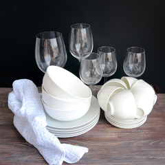 White dishware stacked on a wooden table against black background with transparent wineglasses
