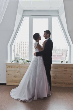 Portrait of the newlyweds embracing against a large window 6456.