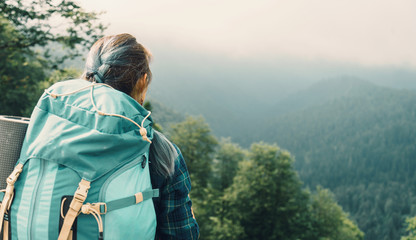Traveler young woman with backpack looking at the mountains in summer, rear view