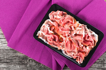 curled slices of delicious Prosciutto on black rectangular dish
