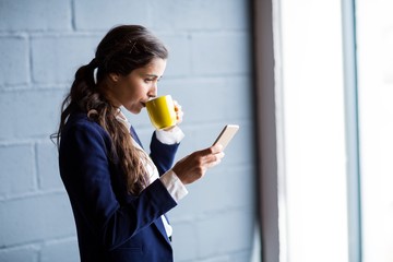 Woman drinking coffee while using phone