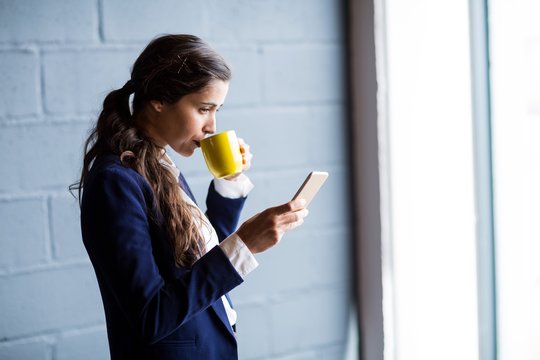 Woman drinking coffee while using phone