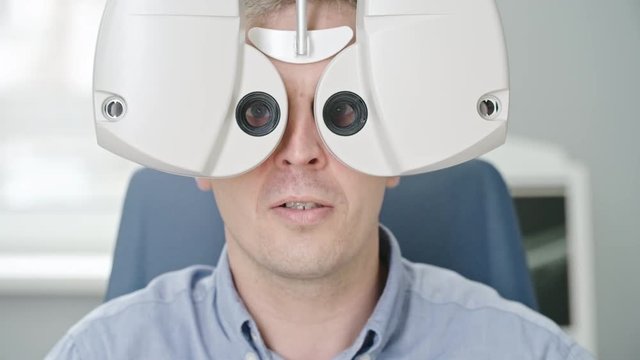 Closeup of mid adult man reading eye chart during distance vision exam with modern digital phoropter