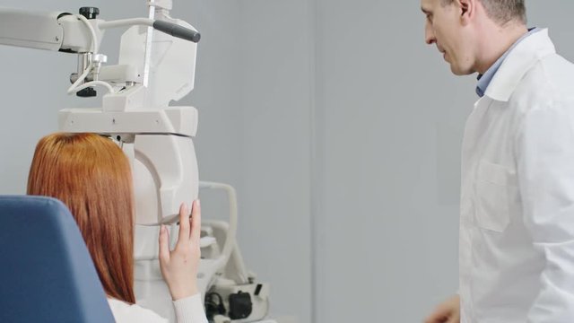 Optometrist using modern equipment to test visual acuity of female patient, woman reading eye chart through digital phoropter