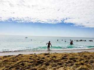 Fototapeta premium Piaszczysta plaża i delikatne fale na morzu, młoda osoba wchodzi do wody