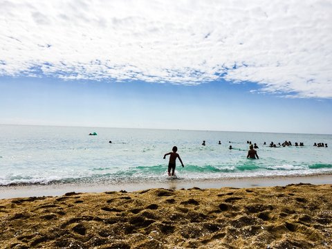 Fototapeta Piaszczysta plaża i delikatne fale na morzu, młoda osoba wchodzi do wody