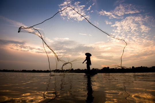 Fisherman throwing net at sunrise , Thailand