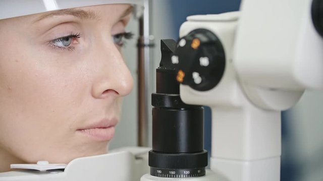 Closeup of beautiful young woman having her eyes examined with biomicroscopic slit lamp device during comprehensive eye exam