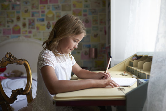 Girl Writing In Notebook While Sitting At Desk