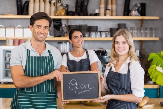 Smiling colleagues showing chalkboard with open sign