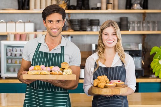 Portrait of waiter and waitress holding a tray of cupcakes