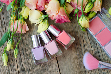 Nail polish, blush and brush on a wooden table on a background of beautiful flowers. Women's cosmetics