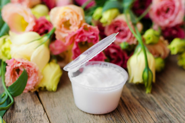 Open a jar of cream on a wooden table on a background of beautiful flowers