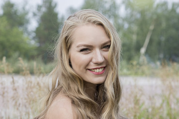 portrait of a cute blonde long-haired caucasian woman standingoutside in a field on a bright  summer day smiling healthy skin sexy