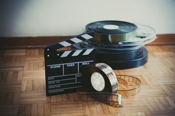 Movie clapper board and film reel on wooden floor