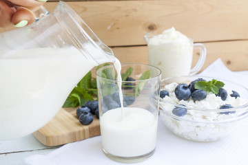 Pouring milk in the glass on the table with other dairy products, bilberry and fresh mint