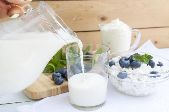 Pouring milk in the glass on the table with other dairy products, bilberry and fresh mint