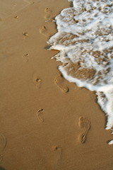 Sea foam waves on the beach washes footprints of adult and kid.