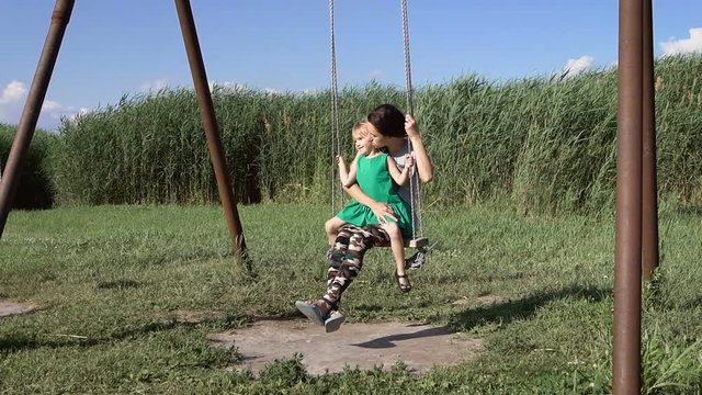 Beautiful young woman with a charming little girl swinging outdoors