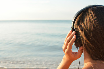 Young woman in headphones listening music and enjoying beautiful views sea, rear view. 