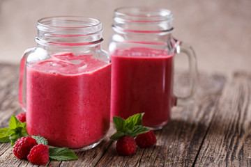 Tasty raspberry smoothie in glass jar on wooden table.