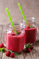 Tasty raspberry smoothie in glass jar on wooden table.