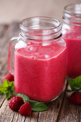 Tasty raspberry smoothie in glass jar on wooden table.