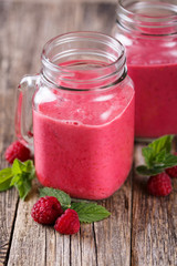 Tasty raspberry smoothie in glass jar on wooden table.