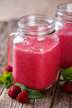 Tasty raspberry smoothie in glass jar on wooden table.