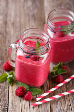 Tasty raspberry smoothie in glass jar on wooden table.