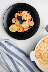 Spaghetti with grilled shrimps on a black plate with lemon and basil