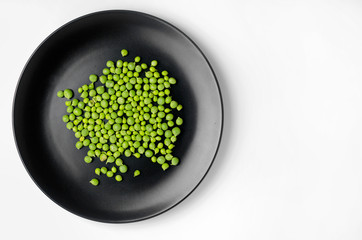 Green peas on a black plate on white table