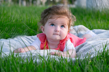 Little girl (six months old) with beautiful blue eyes is lying on the grass in the park. She looks...