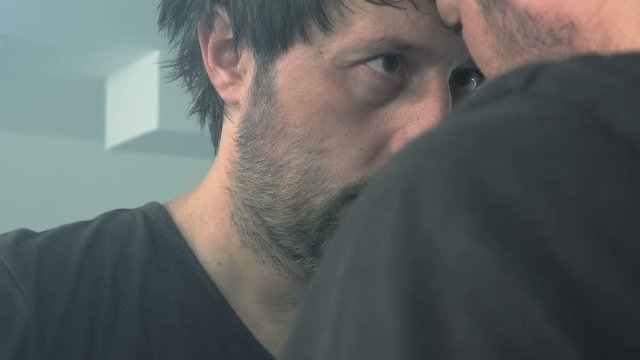Disappointed man looking himself in the mirror, sad and lonely male person feeling depressed with pessimistic face expression.