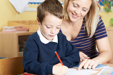 Teacher Helping Male Elementary Pupil Working At Desk