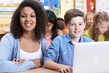 Teacher Helping Male Elementary Pupil In Computer Class