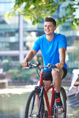 Obraz premium Young Man Cycling Next To River In Urban Setting