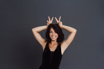 Cute woman posing over grey background and make funny gesture