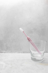 Pink tooth brush inside clear glass with concrete background